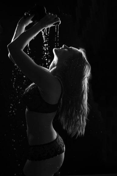 Silhouette einer Frau in Unterwäsche, die Wasser über ihren Kopf gießen lässt.