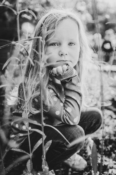 Ein nachdenkliches Kind mit langen Haaren, das in der Natur sitzt.