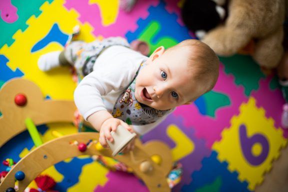 Ein Baby im Spielzimmer greift nach einem Spielzeug auf buntem Boden.