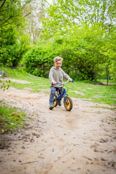 Ein Junge fährt auf einem kleinen Fahrrad auf einem unebenen, grünen Weg.