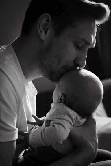 Vater küsst sein Baby auf die Stirn, in einem sanften, liebevollen Moment.