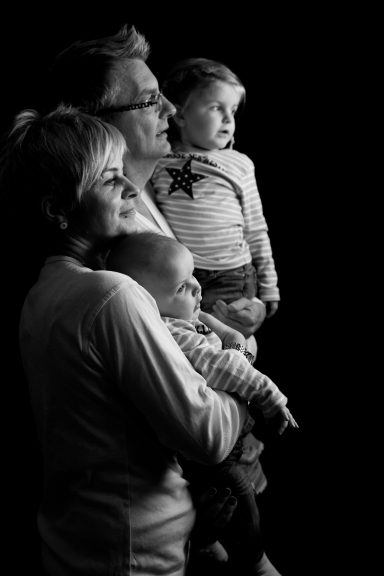 Familie steht zusammen in einer dunklen Umgebung, blickt nachdenklich nach vorne.