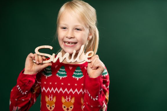 Lächelndes Kind in einem roten Weihnachtspullover hält das Wort "Smile".
