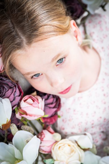 Mädchen mit blonden Haaren liegt umgeben von bunten Blumen.