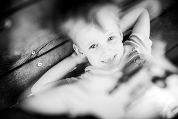 Lächelndes Kind, das entspannt auf einem Holzboden liegt, in Schwarzweiß.