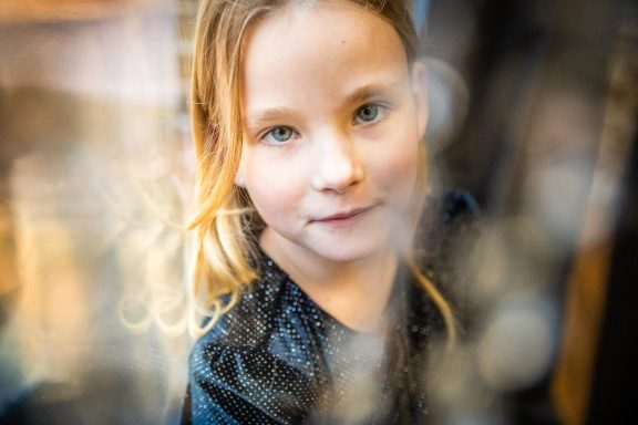 Ein Mädchen mit langen, lockigen Haaren schaut aufmerksam in die Kamera.