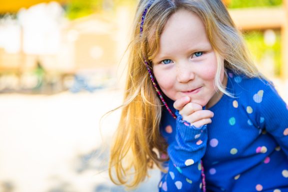Ein kleines Mädchen mit langen blonden Haaren in einem blauen Pullover mit Punkten.