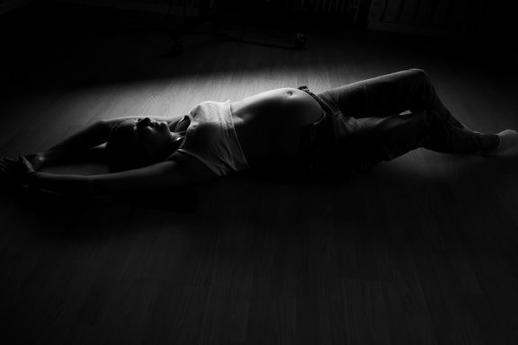 Eine schwangere Frau liegt entspannt auf dem Boden in Schwarz-Weiß.