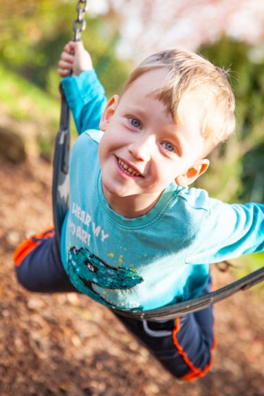 Ein lächelnder Junge schwingt fröhlich auf einer Schaukel im Freien.