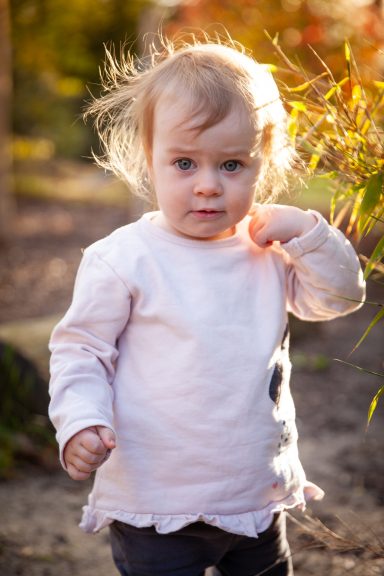 Kleines Kind mit blonden Haaren in einem hellen Pullover, steht im Freien.