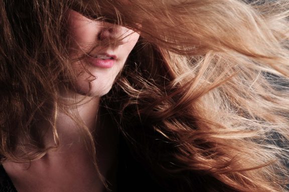 Frau mit langen, weichen, bewegten Haaren vor dunklem Hintergrund.