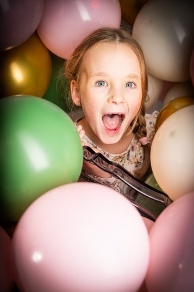 Ein Mädchen mit weit geöffnetem Mund, umgeben von bunten Luftballons.