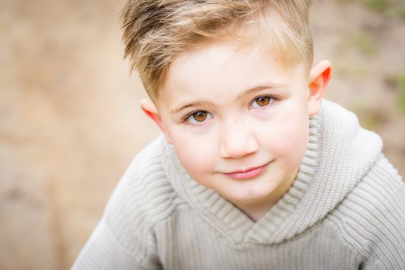Ein junger Junge mit kurzen, blonden Haaren und einem grauen Pullover schaut in die Kamera.