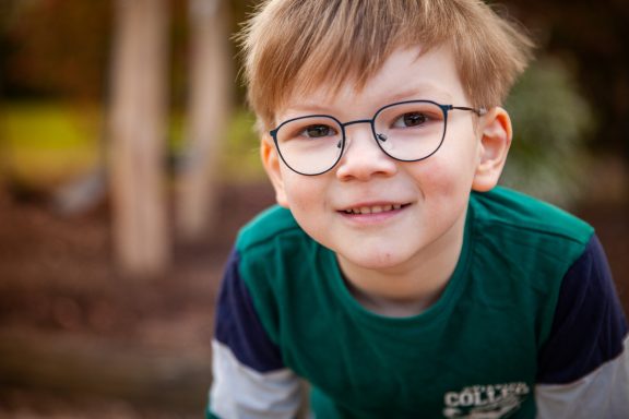 Ein lächelnder Junge mit Brille, der in einem Garten spielt.