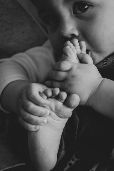 Ein Kleinkind, das neugierig seine eigenen Füße mit Händen hält und an ihnen kaut.