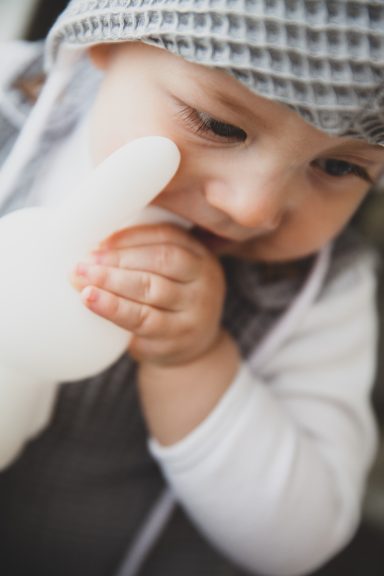 Ein kleines Kind mit einer Mütze hält eine weiße Spielzeugfigur.
