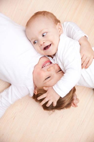 Zwei Kinder liegen spielend auf dem Boden und lachen miteinander.