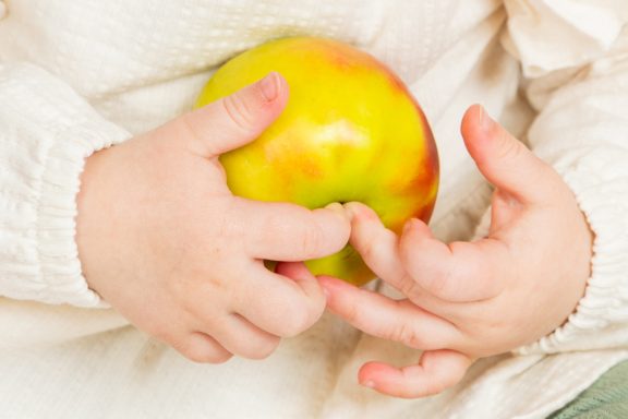 Ein Kleinkind hält einen gelben Apfel in den Händen.