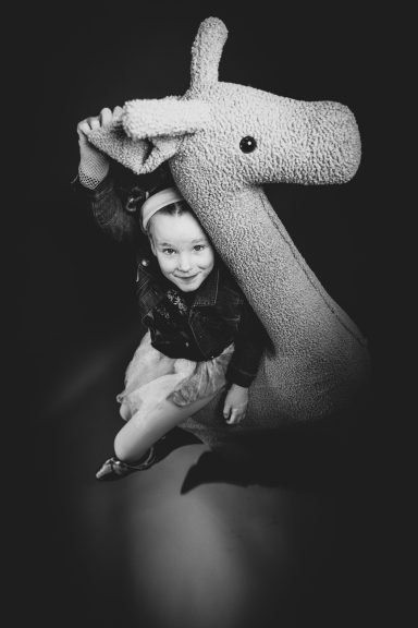 Ein Kind sitzt neben einem großen, plüschigen Giraffenspielzeug.